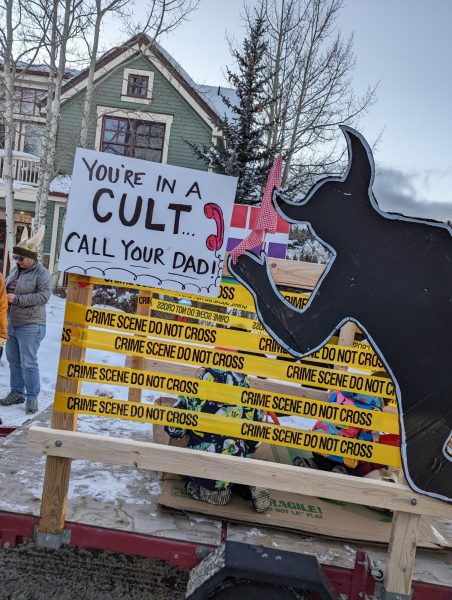 sign with youre in a cult call your dad, some crime scene tape, and the cardboard cut out of a troll made to look like chalk outline of a dead body 