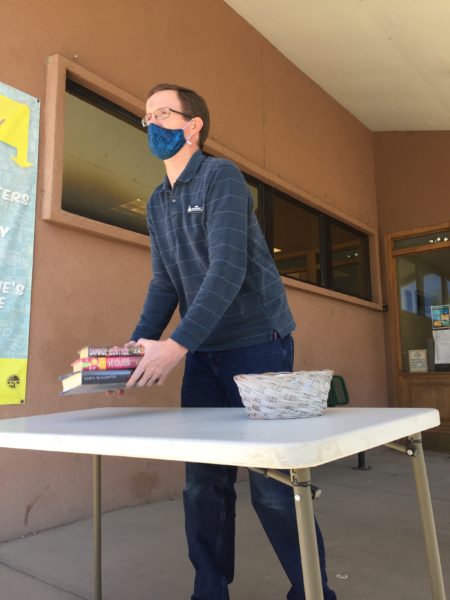 A library worker sets books downs on a table outside the library for curbside delivery to a patron.