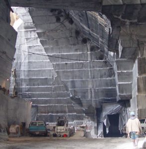 Workman and stone-cutting equipment in front of large step-cut rockface of quarry