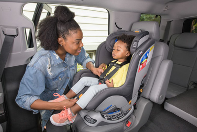 Photograph of a person securing a toddler-aged child into a car seat.
