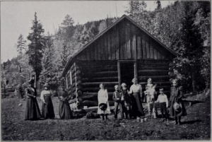 Women and children standing in front of log house in the mountains