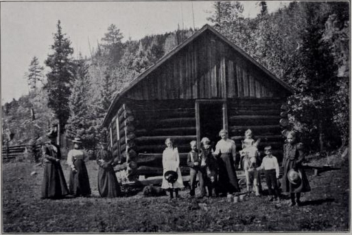 black and white photo of students and teachers outside small log building