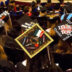 A view of about twenty students facing away from the camera sitting in rows of chairs during a commencement ceremony. The students are wearing black commencement robes. The angle of the photo shows the tops of their decorated graduation caps.