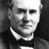 A black and white photographic headshot of Governor Buchtel, who has a serious facial expression and is wearing a black jacket, white shirt, and a black bowtie.
