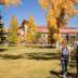 A pair of two students walk away from the viewer across a grassy area towards a red brick university building. The grassy area is dotted with cottonwood trees that have changed to yellow for the fall. Two other small groups of students can be seen walking across the grass in the background.