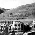 A black and white photograph, featuring condo buildings in the foreground and the snow-free hills of Vail's ski resort in the background.