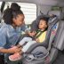Photograph of a person securing a toddler-aged child into a car seat.