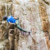 A rock climber hang off the side of a rock wall pauses to reach into a chalk bag.