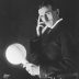 Black and white photo portrait of Nikola Tesla in a dark suit.